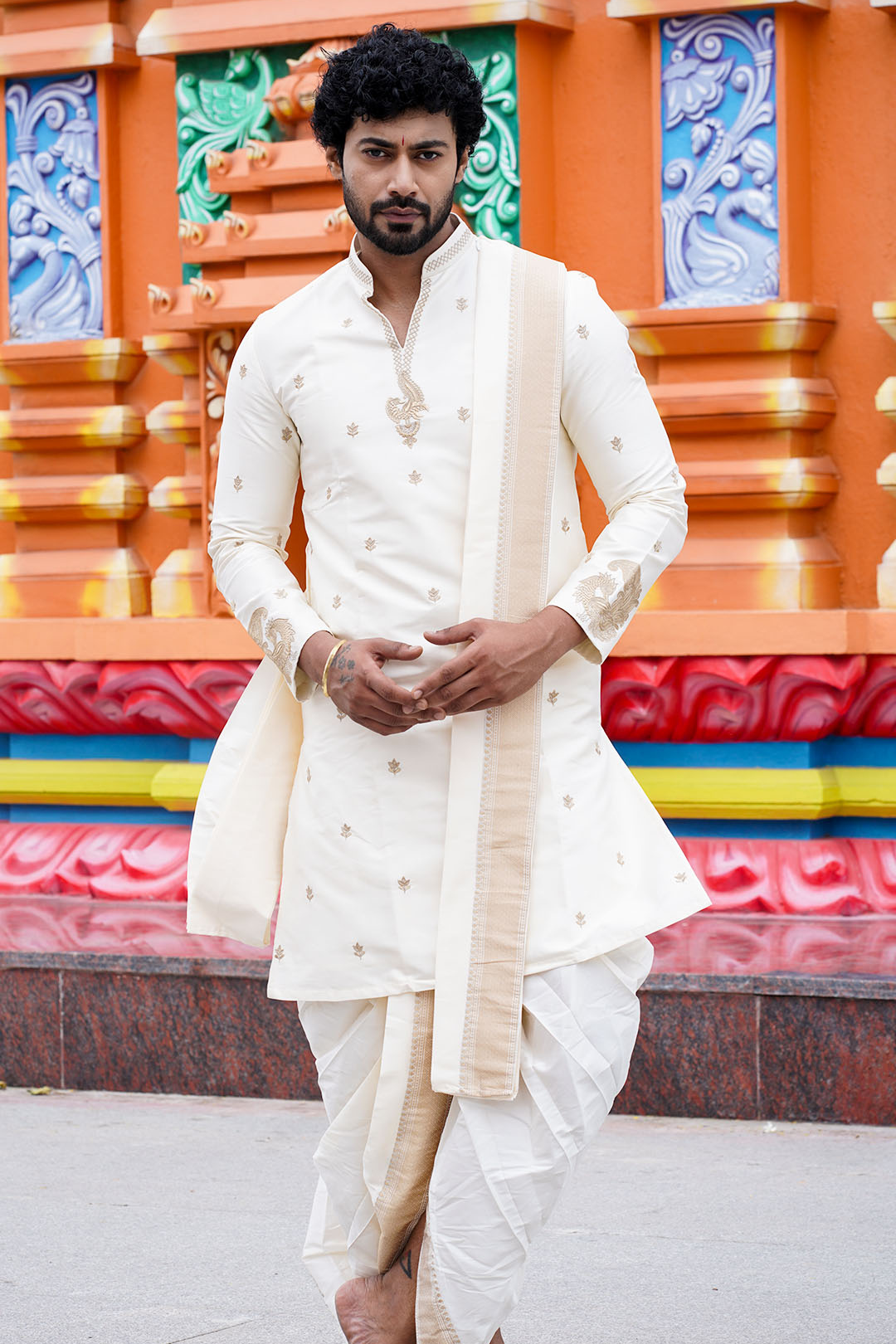 Man in traditional white outfit standing in front of a colorful architectural background
