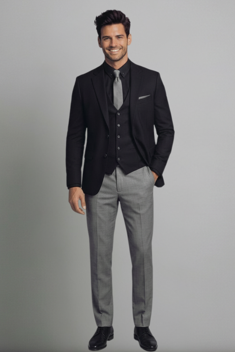 Man wearing a black blazer, gray vest, and gray pants on a gray background