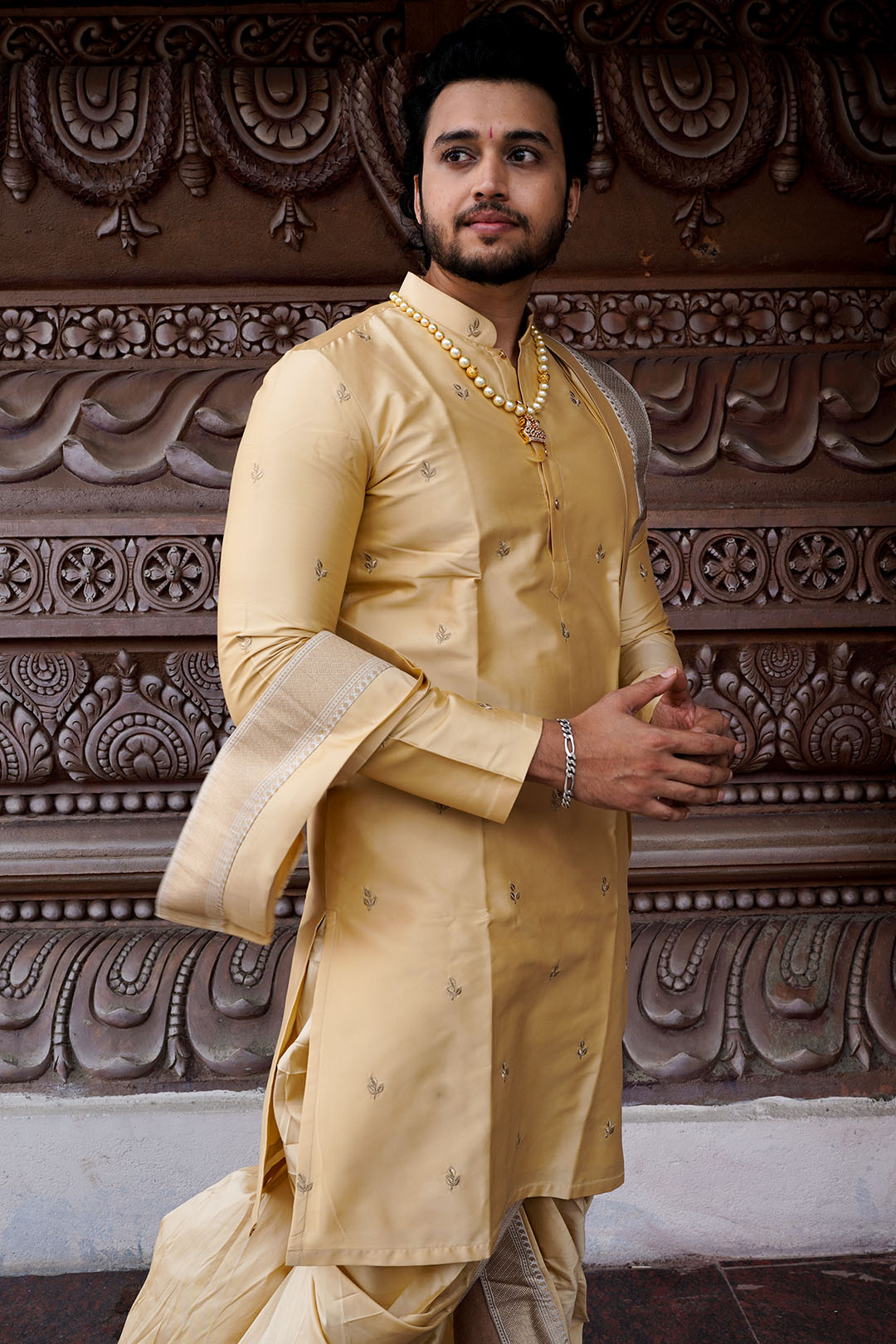 Man wearing a traditional beige kurta with intricate carvings in the background