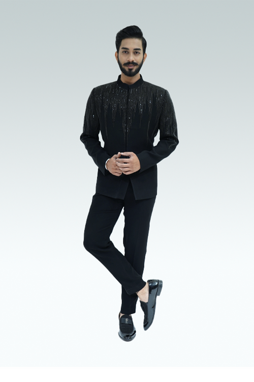 A man wearing a black shirt with wood crepe fabric and embellishments, paired with black trousers.