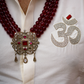 Close-up of a white shirt with a red beaded necklace and an embroidered symbol on a plain background