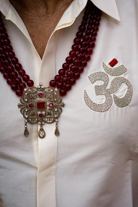 Close-up of a white shirt with a red beaded necklace and an embroidered symbol on a plain background