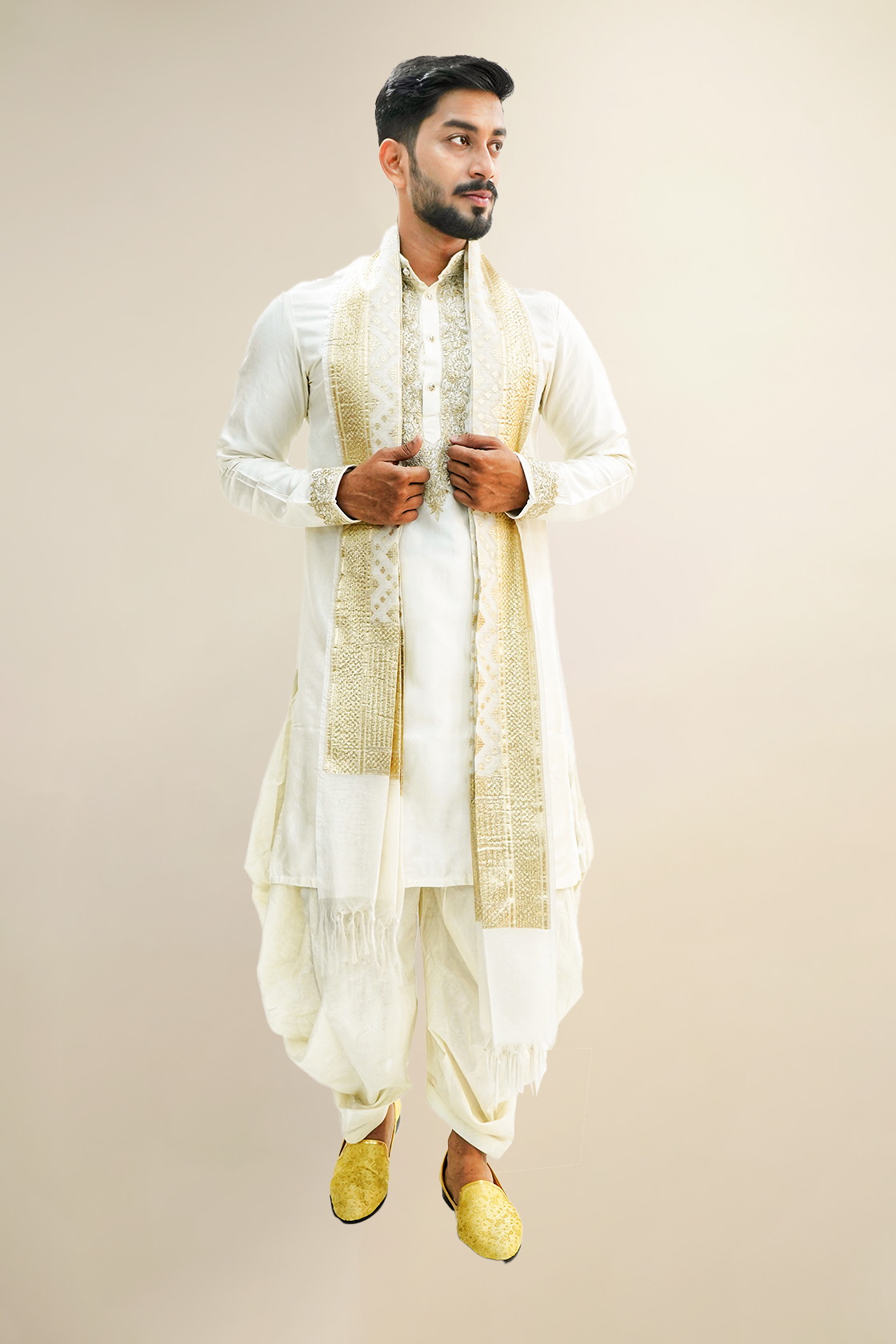 A man wearing an off-white semi-pattu kurta set with zari embroidery, standing against a light background.
