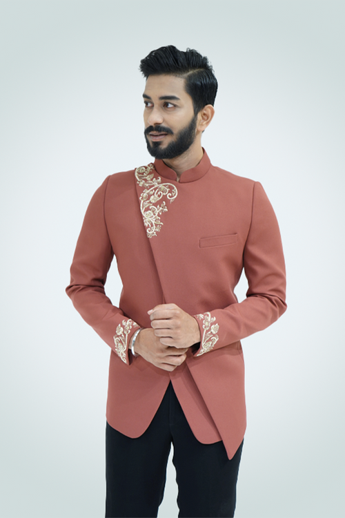 A man wearing a rust-colored Jodhpuri suit with gold embroidery, featuring a mandarin collar and cross cut design.