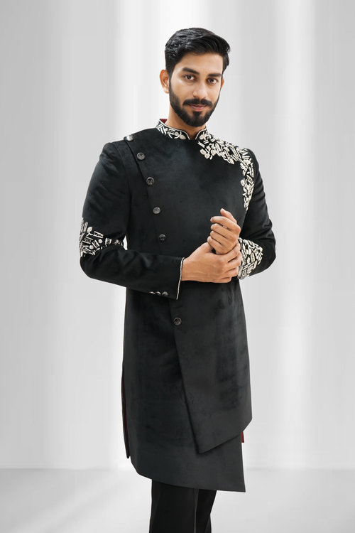 A man wearing a black asymmetrical Indo-Western sherwani with silver zardozi work on the sleeves and chest.