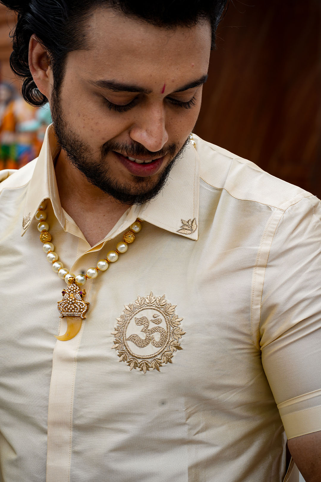 Man wearing a cream-colored traditional outfit with intricate designs and a necklace.