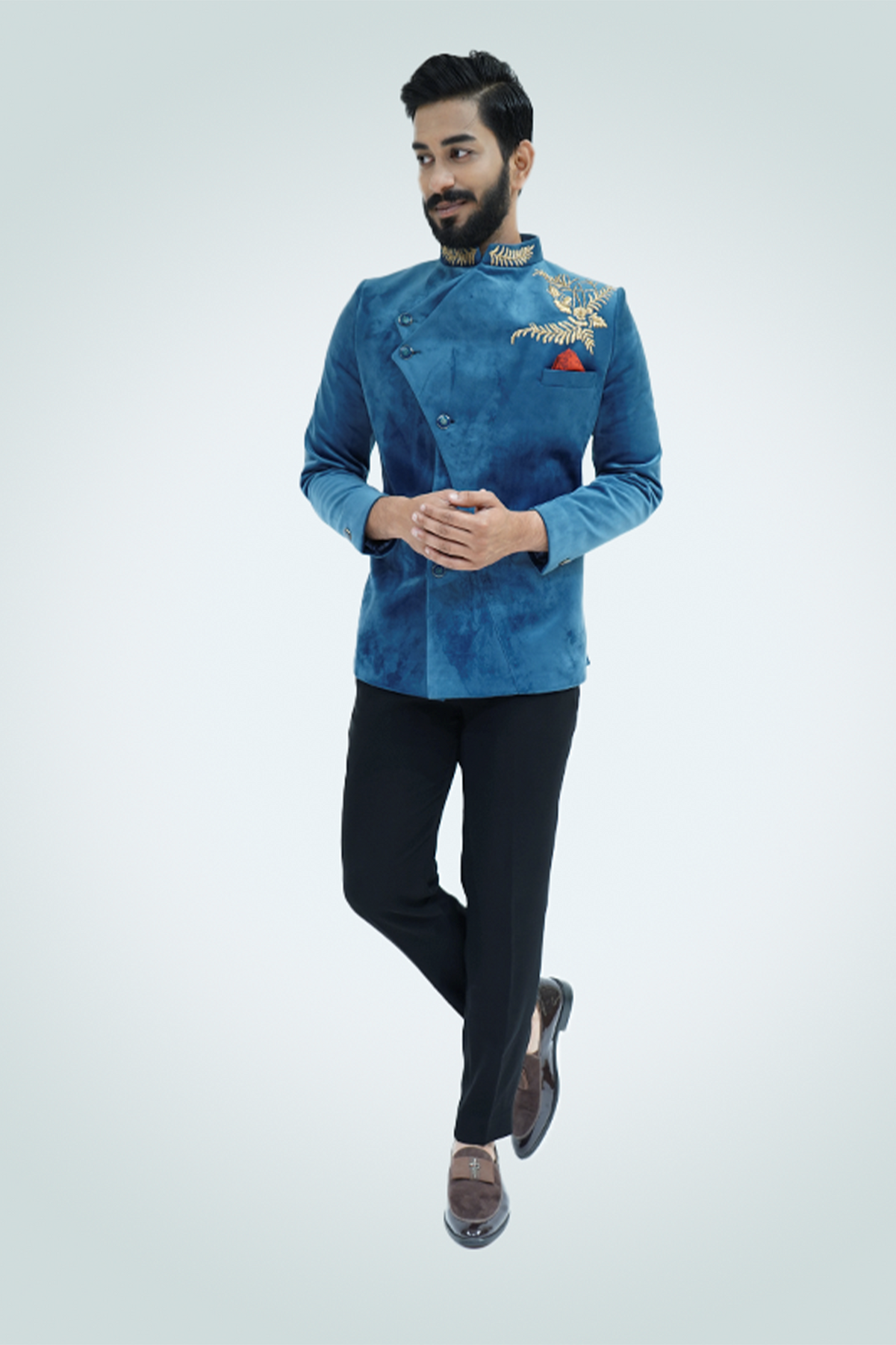 A man wearing a Teal Blue Velvet Jodhpuri with gold embellishments, paired with black trousers and tan shoes.