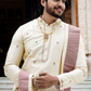 Man in traditional offwhite attire standing in front of a decorative entry.