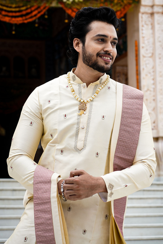 Man in traditional offwhite attire standing in front of a decorative entry.