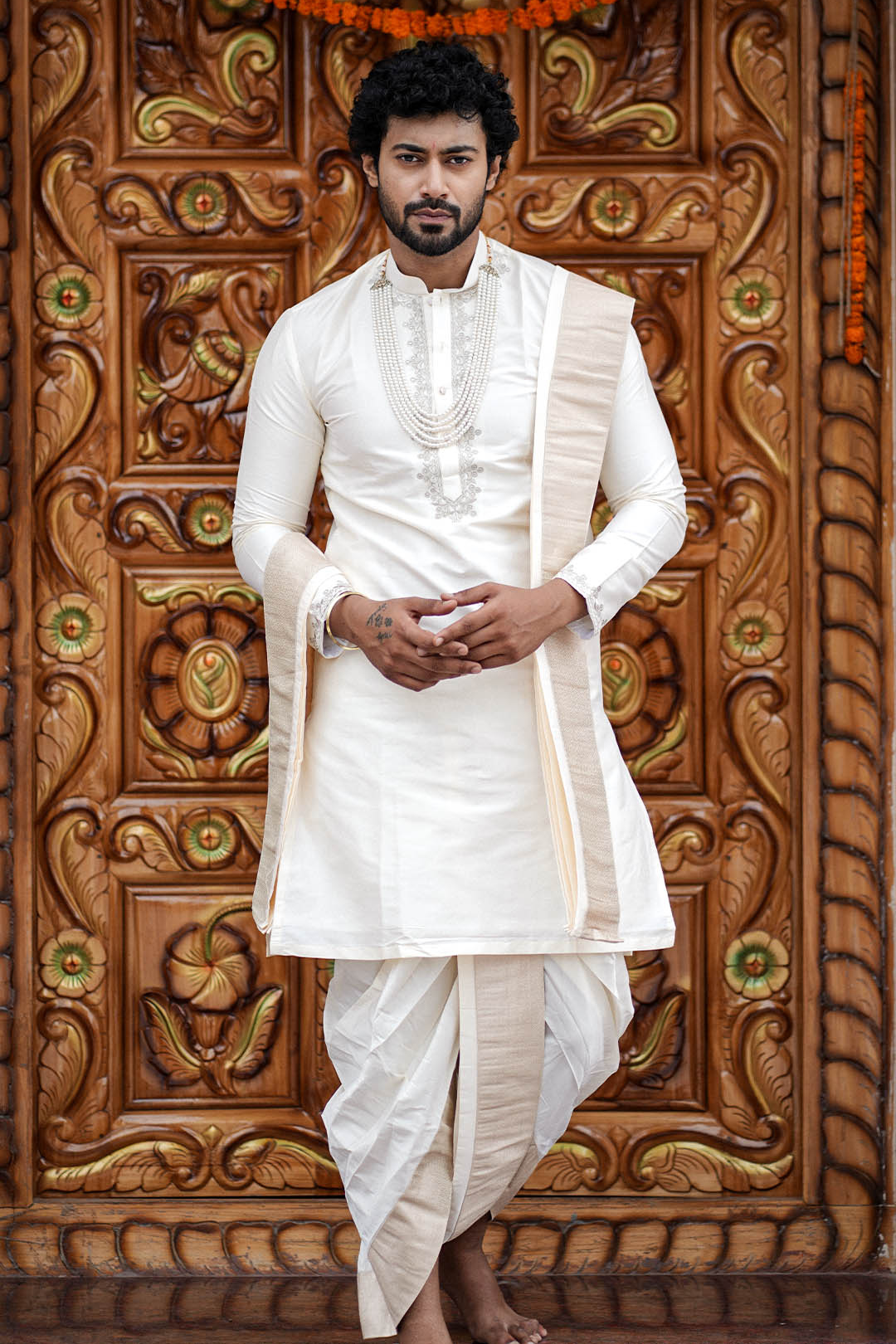 Man in traditional white attire standing in front of a decorative wooden door.