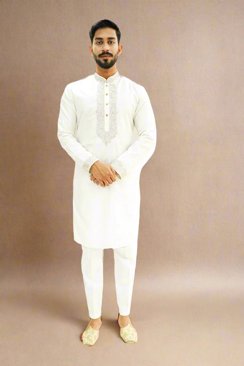 A man wearing an off-white semi-pattu kurta with zari embroidery, standing against a beige background.