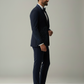 Man wearing a navy suit standing against a plain background