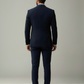 Man wearing a navy suit standing against a plain background