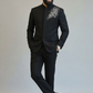 Man wearing a black suit with floral embroidery on a plain background