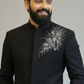 Man wearing a black embroidered jacket against a gray background