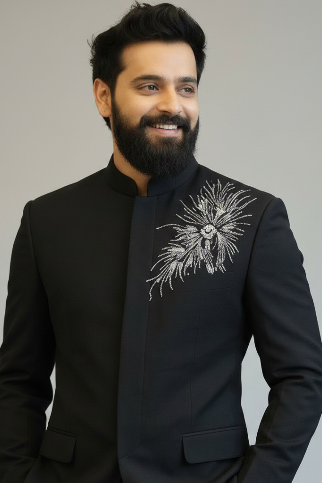 Man wearing a black embroidered jacket against a gray background