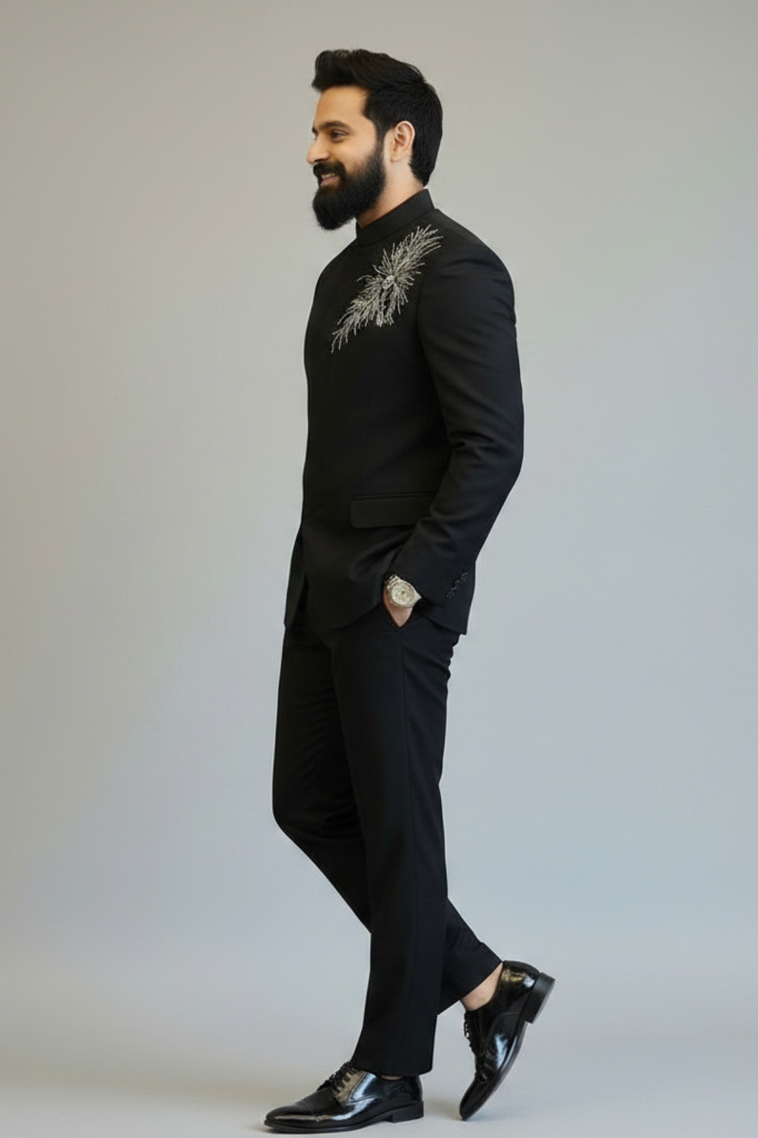 Man wearing a black suit with embroidery on a plain background