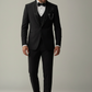 Man wearing a black tuxedo with a white shirt and black bow tie on a plain background