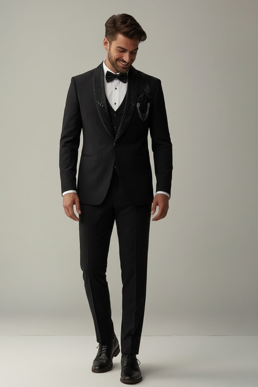Man wearing a black tuxedo with a white shirt and black bow tie on a plain background
