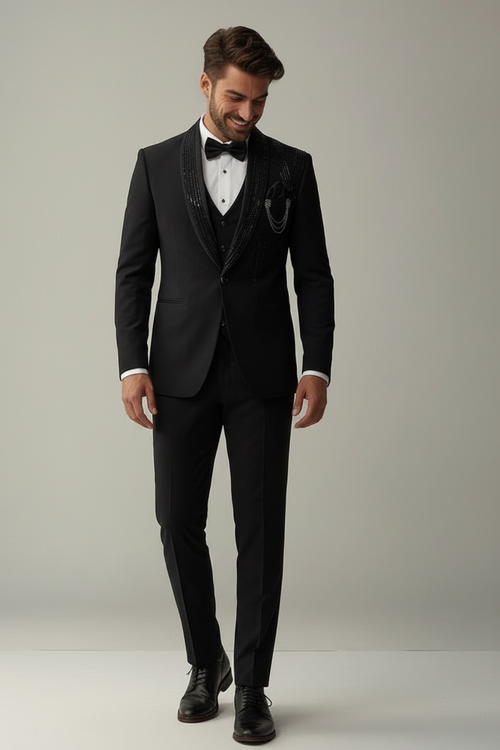 Man wearing a black tuxedo with a white shirt and black bow tie on a plain background