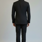 Person wearing a black suit standing against a plain background