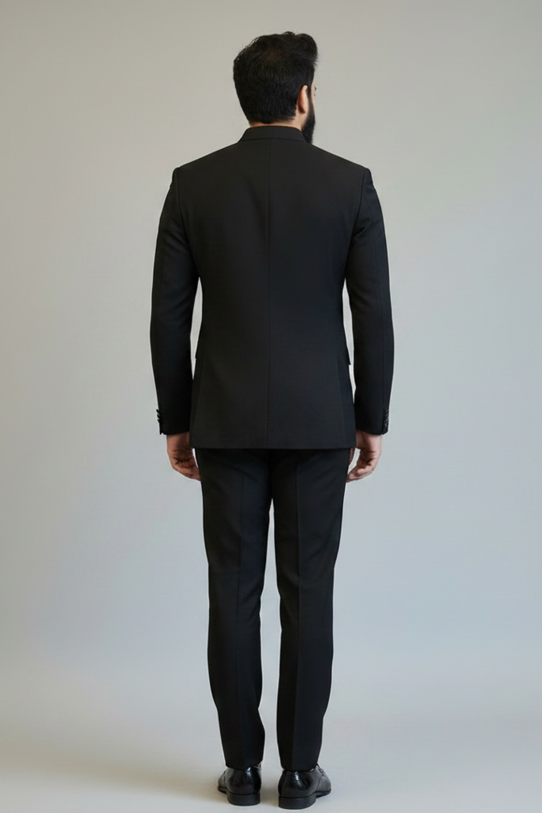 Person wearing a black suit standing against a plain background