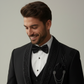 Man wearing a black tuxedo with a bow tie against a plain background