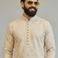 Man wearing a beige embroidered kurta with sunglasses on a gray background