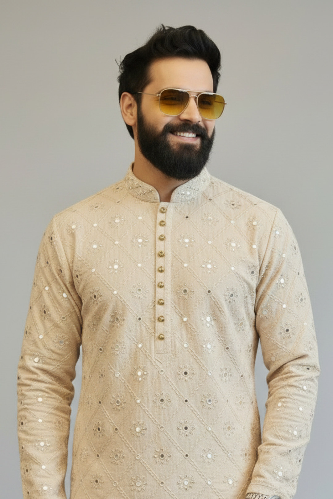 Man wearing a beige embroidered kurta with sunglasses on a gray background