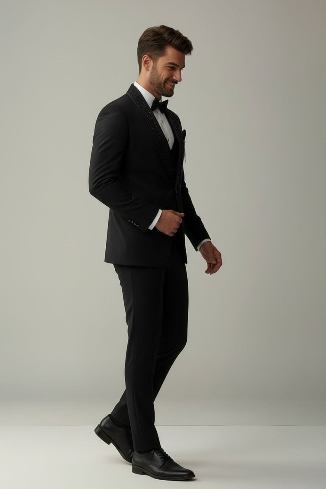 Man wearing a black suit and bow tie on a plain background