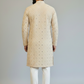 Man wearing a beige embroidered kurta with white pants on a plain background