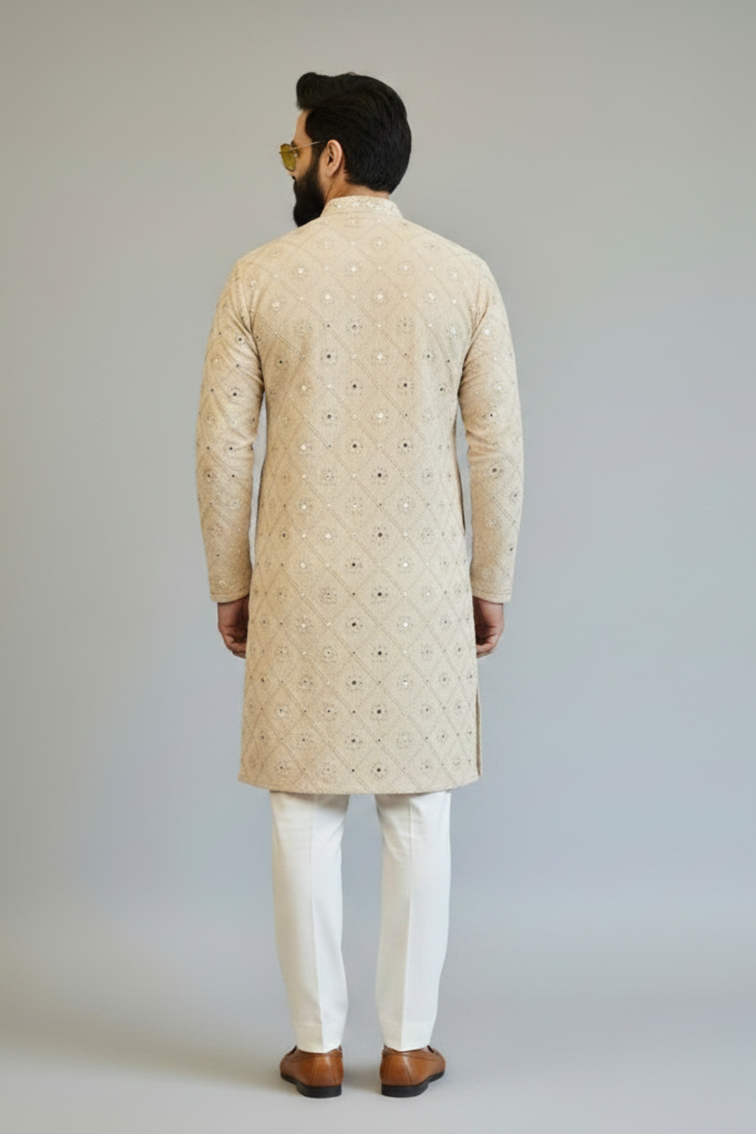 Man wearing a beige embroidered kurta with white pants on a plain background