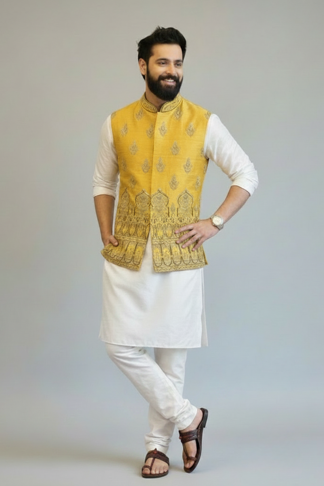 Man wearing a yellow embroidered vest over a white kurta with white pants on a gray background