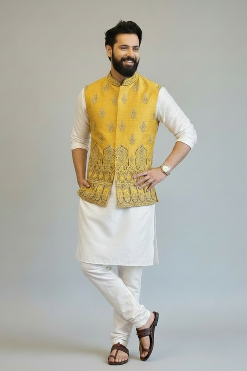 Man wearing a yellow embroidered vest over a white kurta with white pants on a gray background
