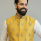 Man wearing a yellow embroidered vest over a white kurta with white pants on a gray background