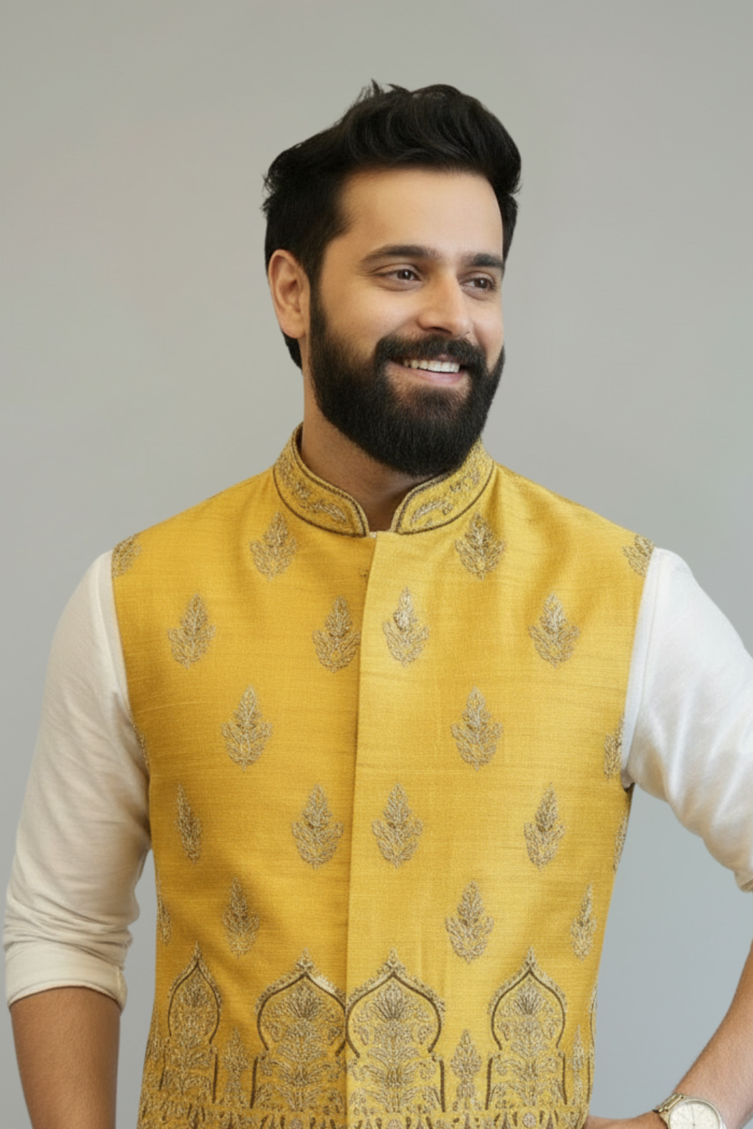 Man wearing a yellow embroidered vest over a white kurta with white pants on a gray background