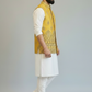 Man wearing a yellow embroidered vest over a white kurta with white pants on a gray background