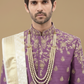 Man wearing a purple embroidered sherwani with a white stole against a beige background