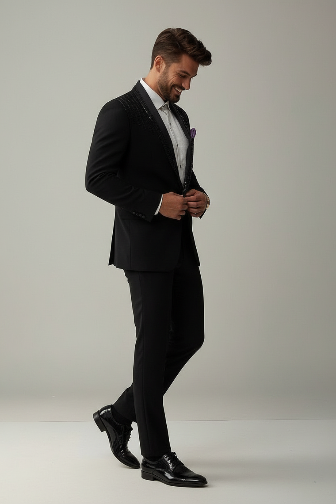 Man in a black suit adjusting his jacket against a plain background