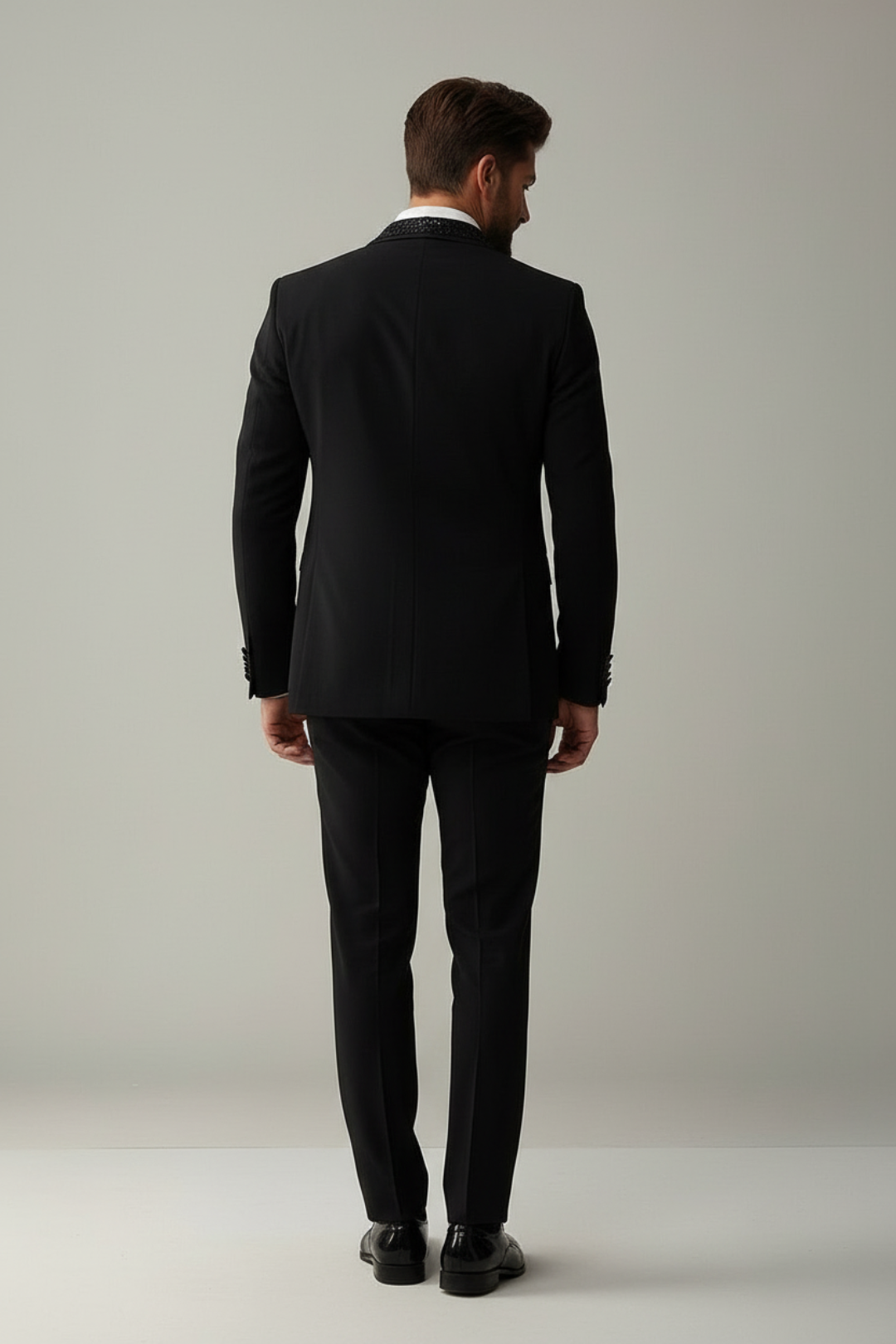 Man wearing a black suit standing against a plain background