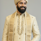 Man wearing a traditional beige sherwani with a turban on a gray background