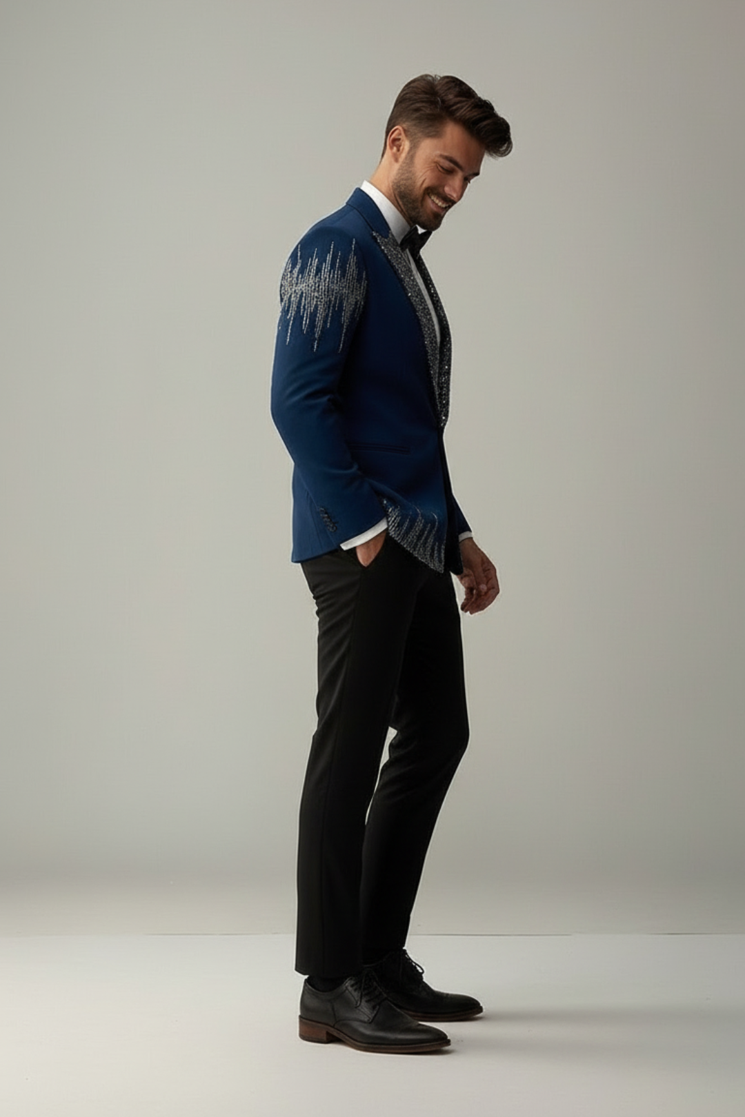 Man wearing a blue blazer with a patterned shirt and black pants on a plain background