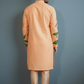 Man wearing an orange kurta with green patterns against a gray background