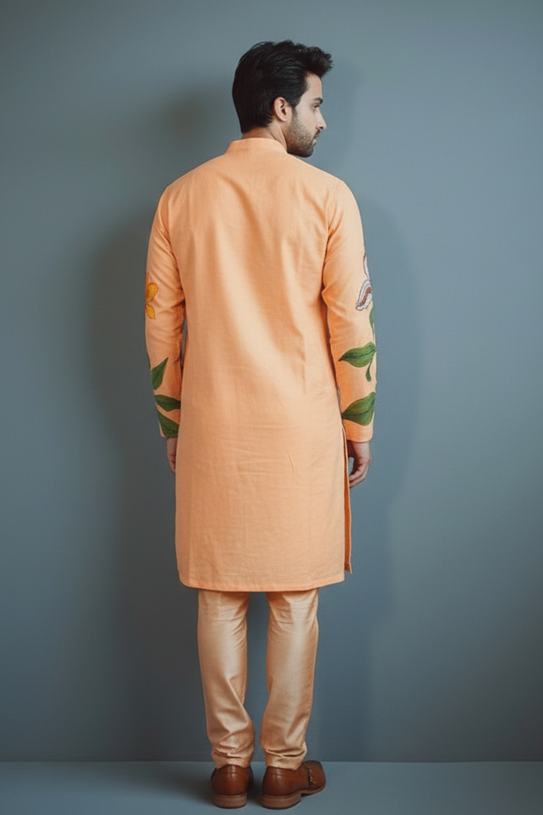 Man wearing an orange kurta with green patterns against a gray background