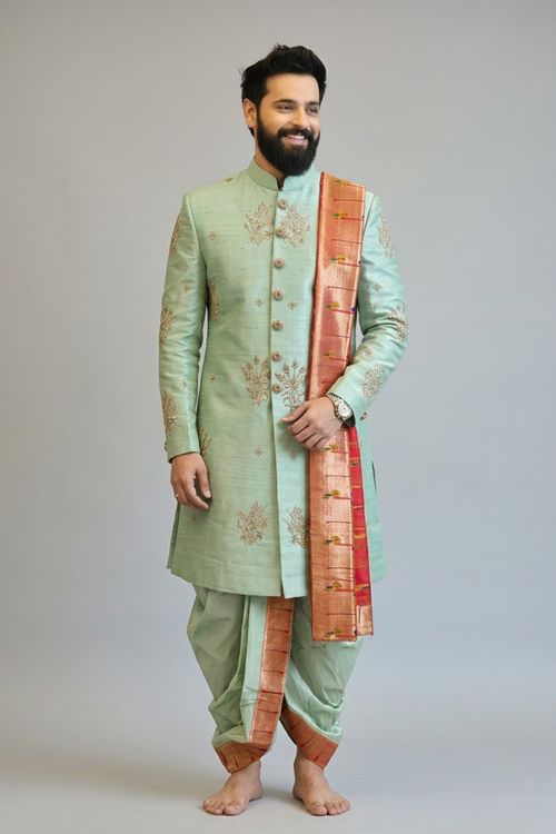 Man wearing a light green sherwani with a red and gold dupatta on a plain background