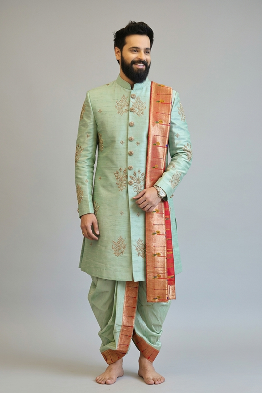Man wearing a light green sherwani with a red and gold dupatta on a plain background