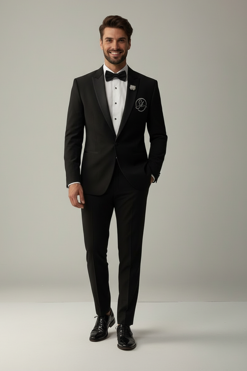 Man wearing a black tuxedo with a white shirt and bow tie on a plain background