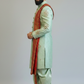 Man wearing a traditional light green sherwani with a red dupatta on a plain background