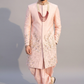 Man wearing a traditional pink sherwani with intricate designs on a gray background