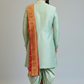 Man wearing a light green sherwani with a red and gold dupatta on a plain background